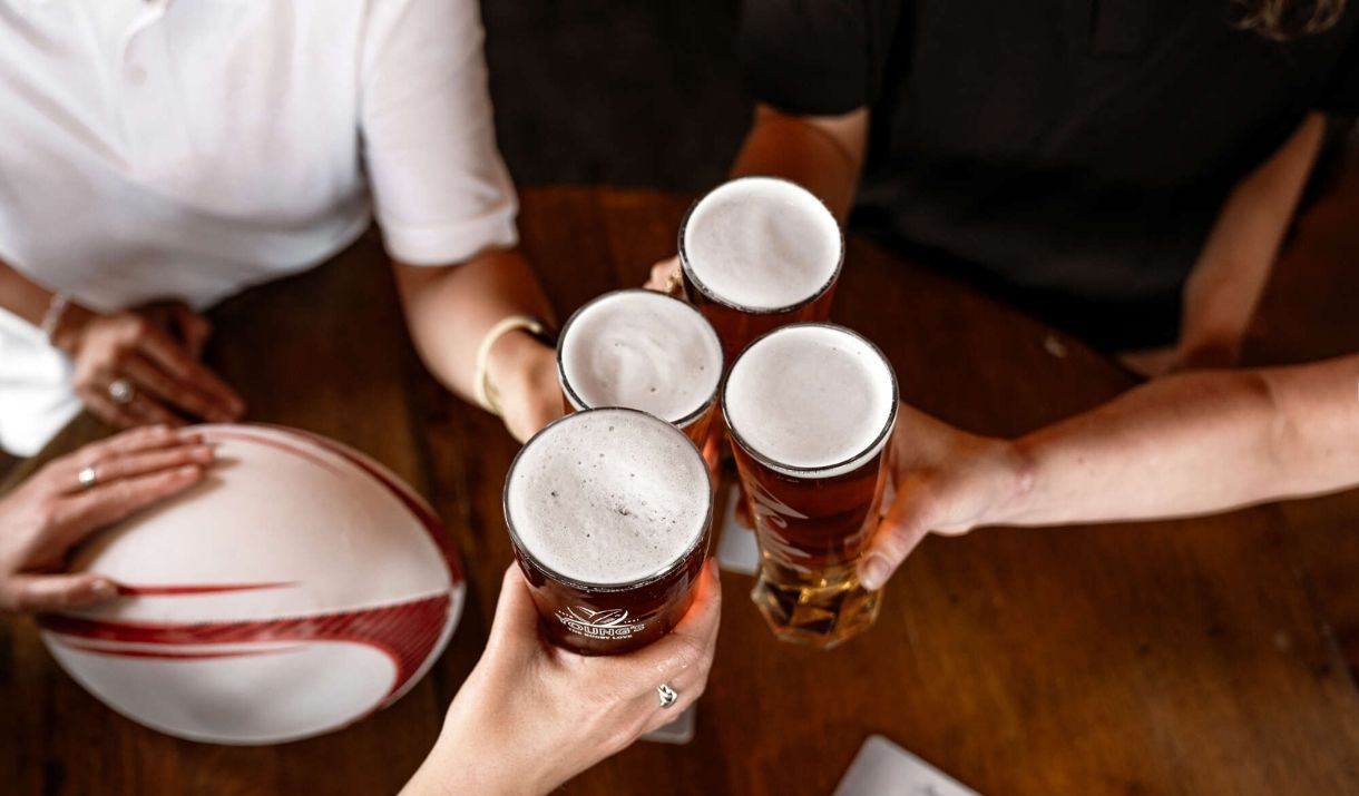 4 people cheersing a pint each, with a rugby ball on the table